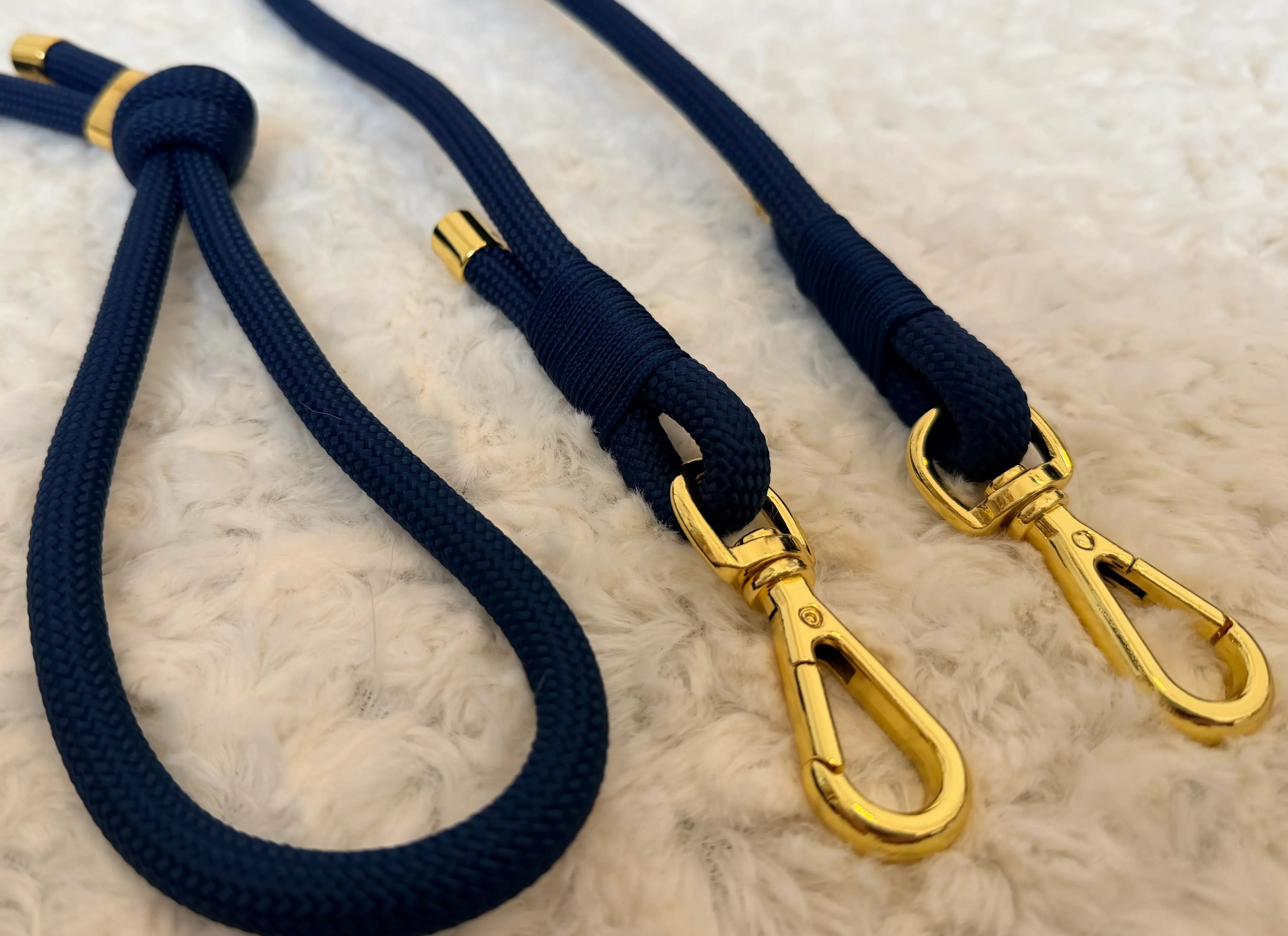 Navy blue dog leash with gold metal clips on white fluffy surface, stylish pet accessory