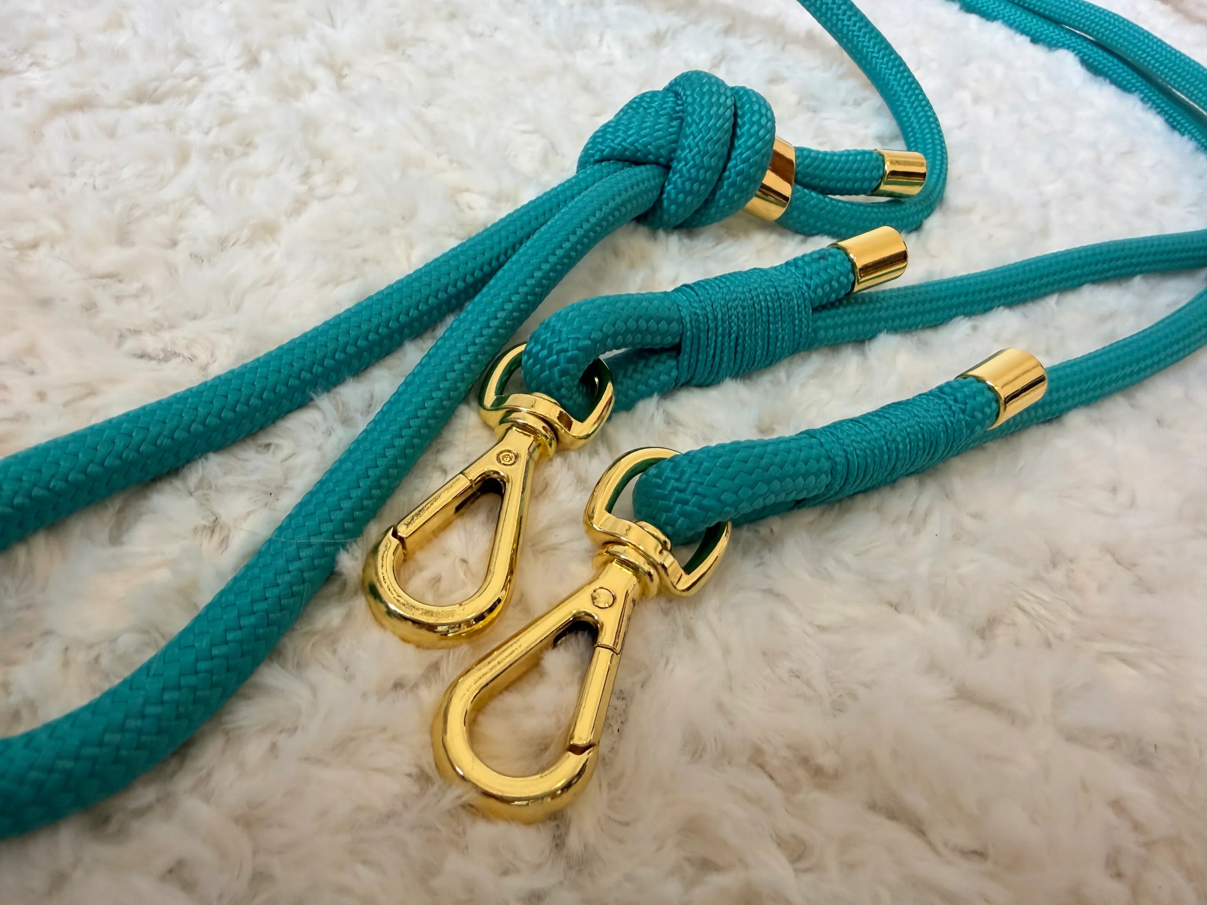 Turquoise braided dog leashes with gold metal clips on soft white textured fabric