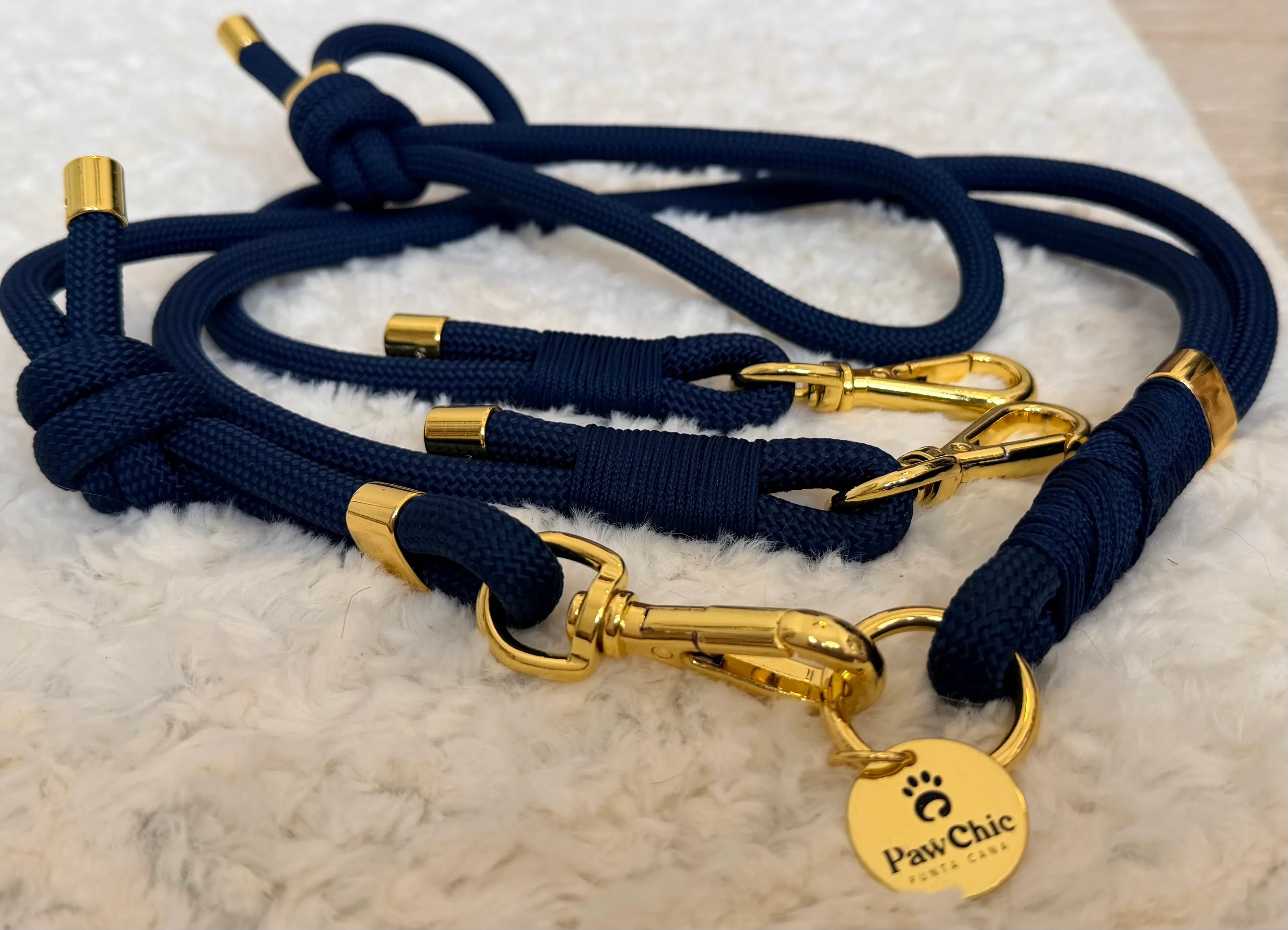 Navy blue rope dog leash with gold metal hardware and tag on soft white textured surface