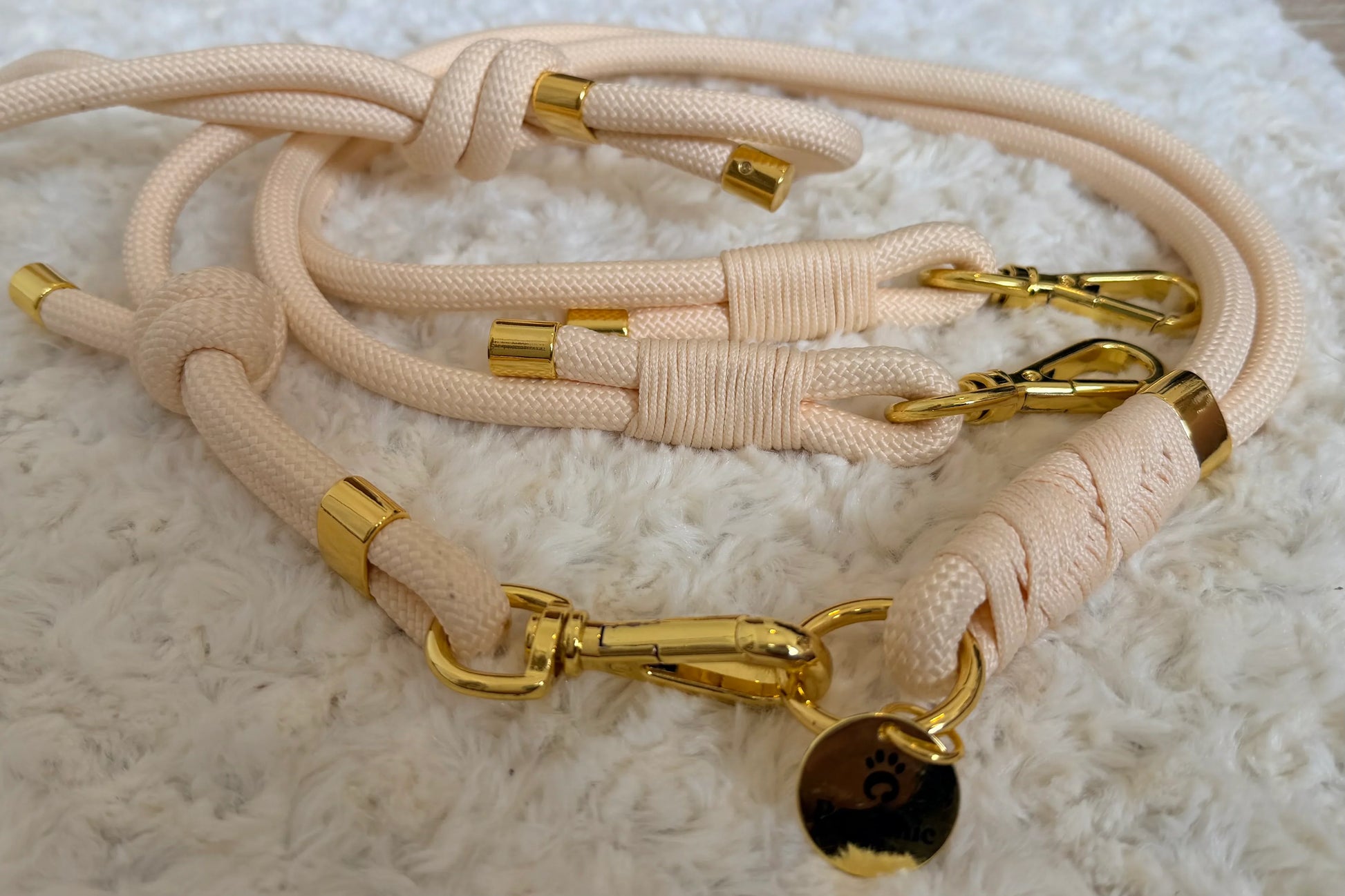 Beige rope dog leash with gold hardware and tag on a white fluffy surface