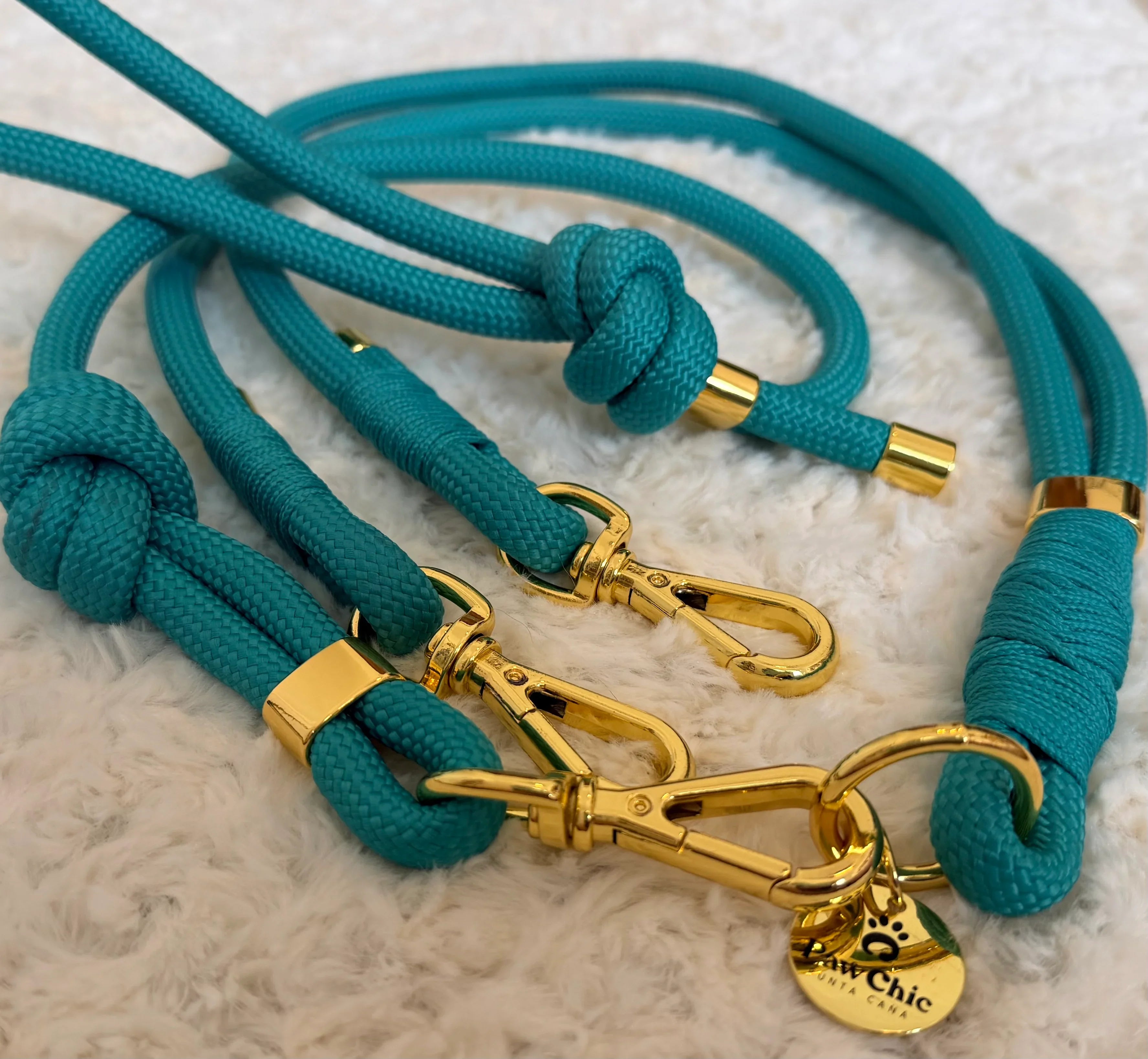 Turquoise dog leashes with gold hardware and knots on a soft white surface